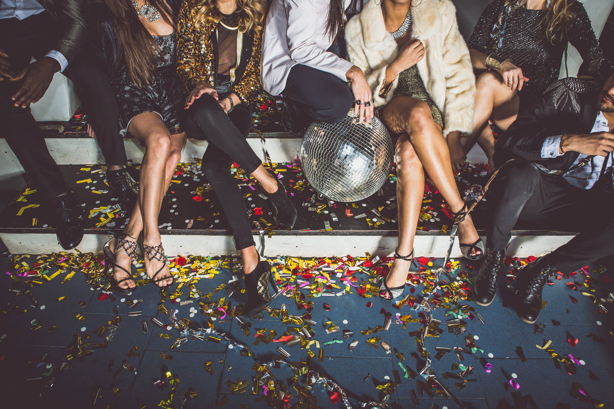An image of a peoples legs dressed in Holiday outfits with confetti and a disco ball.