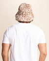 Person wearing a white t-shirt and a tan leopard print bucket hat against a beige background