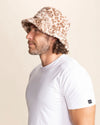 Man wearing a leopard print patterned bucket hat and white t-shirt against a beige background