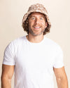 Man wearing a tan leopard print bucket hat and white t-shirt against a beige background