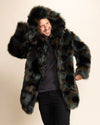Man wearing a fluffy multicolor green, brown, and black faux fur jacket with a hood on a beige background