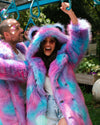 A joyful dark-haired girl wearing sunglasses hangs on the monkey bars with the hood and ears up on her Cotton Candy Bear faux fur coat.