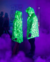 Two people wearing SpiritHoods Neon Green Leopard UV Blacklight Activated Fake Fur Coats, glowing under blacklight, looking at each other, with fog coming up from the dance floor. Halloween Costume Party. halloween costume ideas.