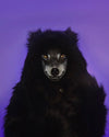 A woman with a wolf painted over her face covering her eyes and mouth to look like a real wolf, in SpiritHoods Classic Black Wolf Faux Fur Coat with the hood up showing black wolf ears on top.