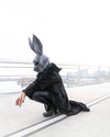 A woman wearing SpiritHoods Classic Black Panther Long Floor Length Fake Fur Jacket, bent down, wearing a large oversized rabbit mask. Easy Halloween Costume Ideas for Women. Halloween outits