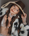 Woman wearing a cowboy hat and SpiritHoods Manx Cat Collector Edition Faux Fur coat with braided hair playing with a lasso around her hat, against a dark background. Easy Halloween Costume Ideas for Women. halloween outfits.
