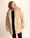 Man wearing a beige faux fur SpiritHoods Cougar coat against a plain background, looking over his shoulder, smiling, feeling confident in his fresh layers.