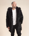 A guy is looking off into the distance with one hand in the pocket of his vegan black wolf coat, the hood down.