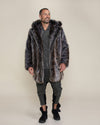 Shorthaired male model with short beard and mustache smiling while looking off in the distance wearing grey wolf fake fur jacket with hood down and hands to his sides.