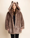 Woman smiling at the camera wearing a over-sized brown fake fur coat with a hood  and wolf ears on a beige background. SpiritHoods Italian Wolf Faux Fur Collector Edition Coat for Women