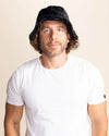 Man wearing a black furry bucket hat and white t-shirt against a beige background