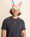 Man wearing a black t-shirt and colorful bunny ears against a beige background