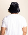Person wearing a black fuzzy bucket hat from behind on a beige background