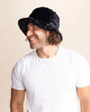 Man wearing a black furry bucket hat against a beige background