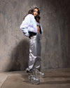 Woman in SpiritHoods Summer Crop Jacket in Mermaid Kitty paired with a futuristic outfit with silver pants and platform boots against a textured wall.