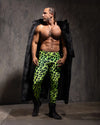 Man wearing neon green leopard print velvet leggings with a black faux fur coat over his shoulder against a gray background