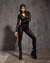 Model wearing a black lace bodysuit with snakeskin pattern with high boots against a textured gray background
