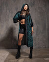 Woman wearing a long emerald green and black tiger print hooded kimono over a black outfit against a gray textured wall.