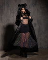 Model wearing a long floor length black fake fur coat with hood andears and colorful skirt against a dark background