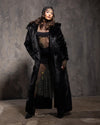 Female Model wearing a long black fake fur duster coat and black sparkling dress with sheer elements against a textured gray background