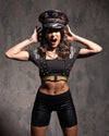 Woman in a black outfit with gold accents and a decorative red sequin leopard print captain's hat with jewels and spikes against a textured gray background
