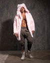 A Man wearing a pink fake fur coat with hood and ears and gray pants against a dark background