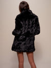 Brown haired girl with her back completely facing the camera wearing  vegan fur black panther coat with a collar.