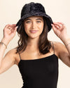 Woman wearing a black leopard print fuzzy bucket hat against a beige background