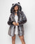 Female model standing in front of a white background wearing a white mini dress and a woman’s faux fur coat with a hood and animal ears.