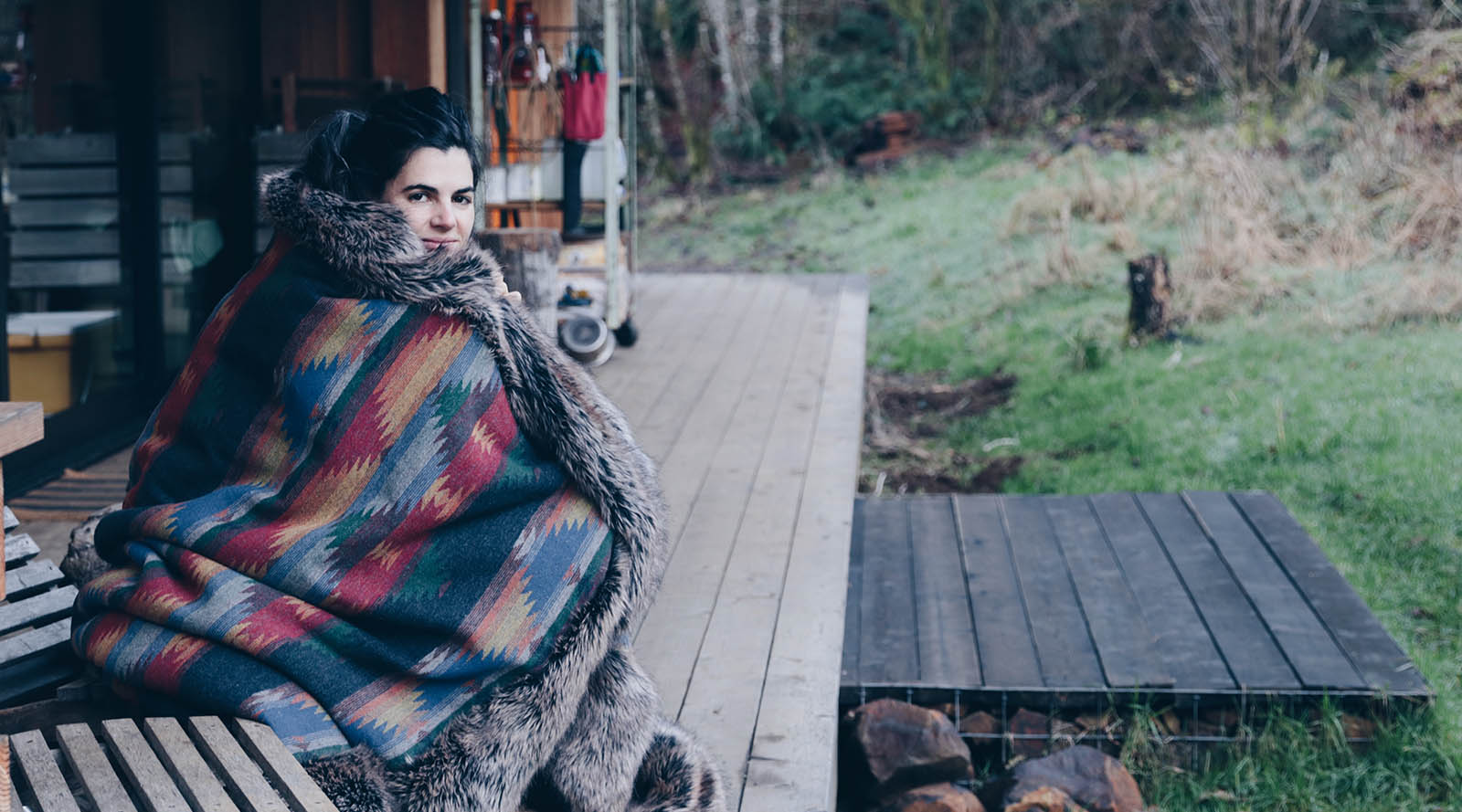 woman sitting outside cabin wrapped in faux fur throw