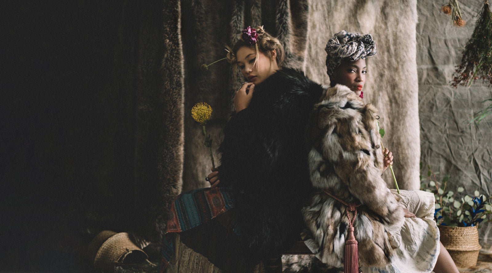 two women sitting back to back wearing faux fur