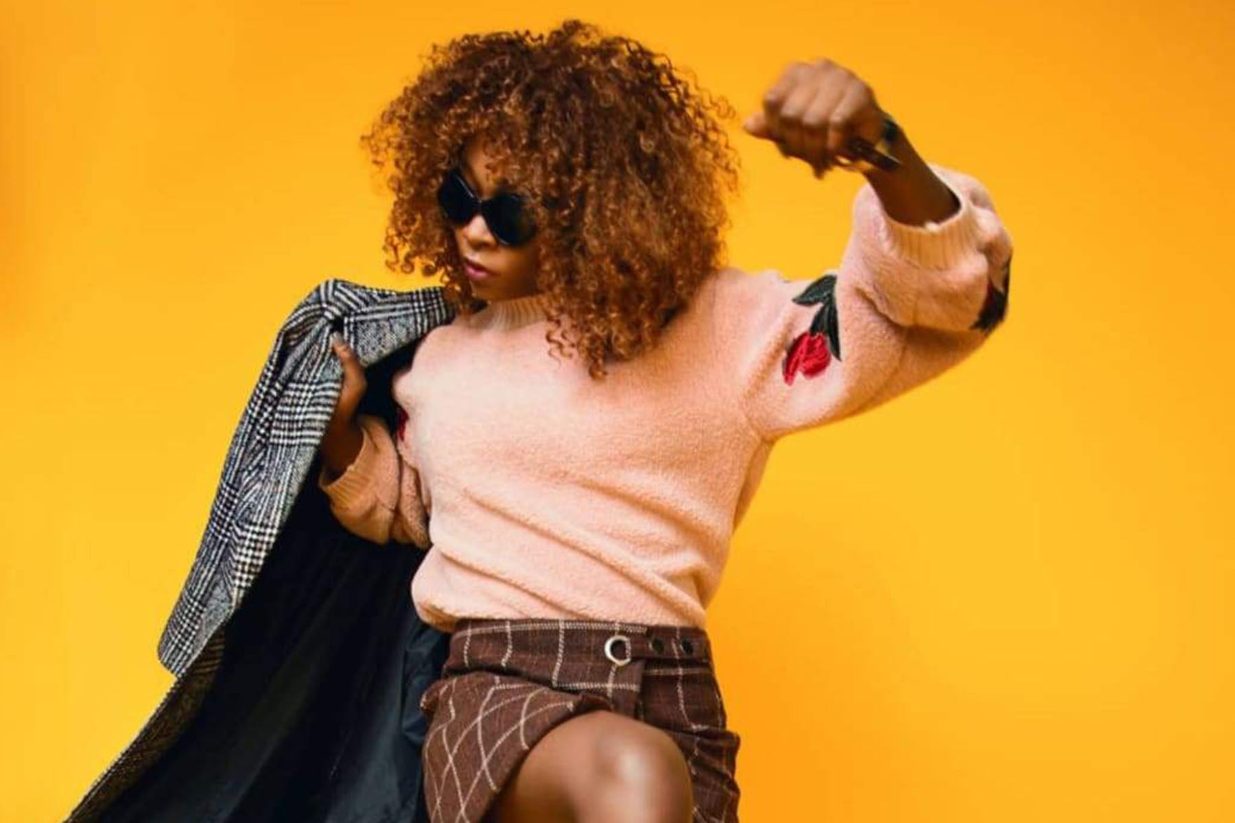 woman holding coat and wearing shirt, skirt, and sunglasses