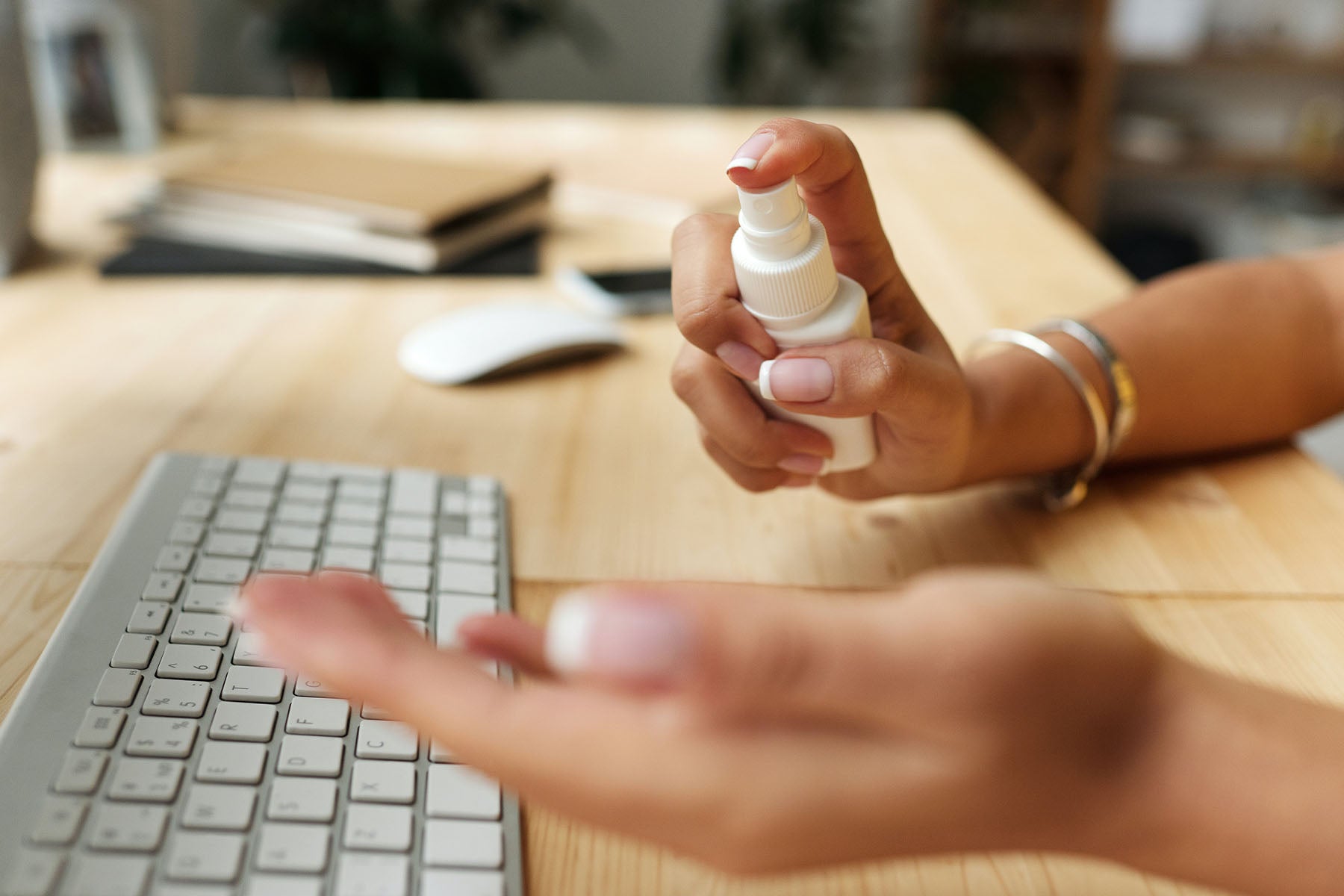 person using spray hand sanitizer on her heads while sitting at desk