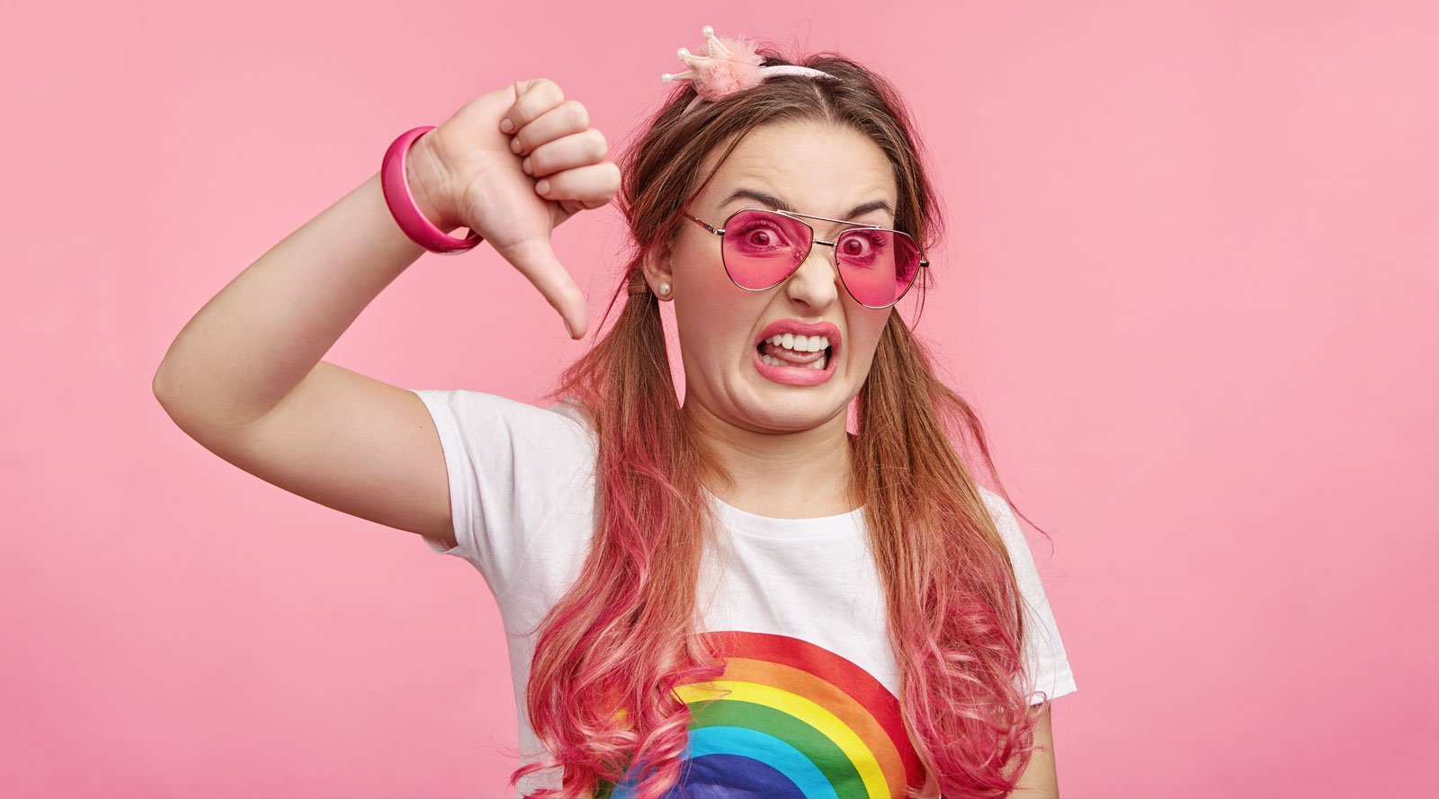 girl with red hair and sunglasses wearing rainbow shirt putting her thumb down