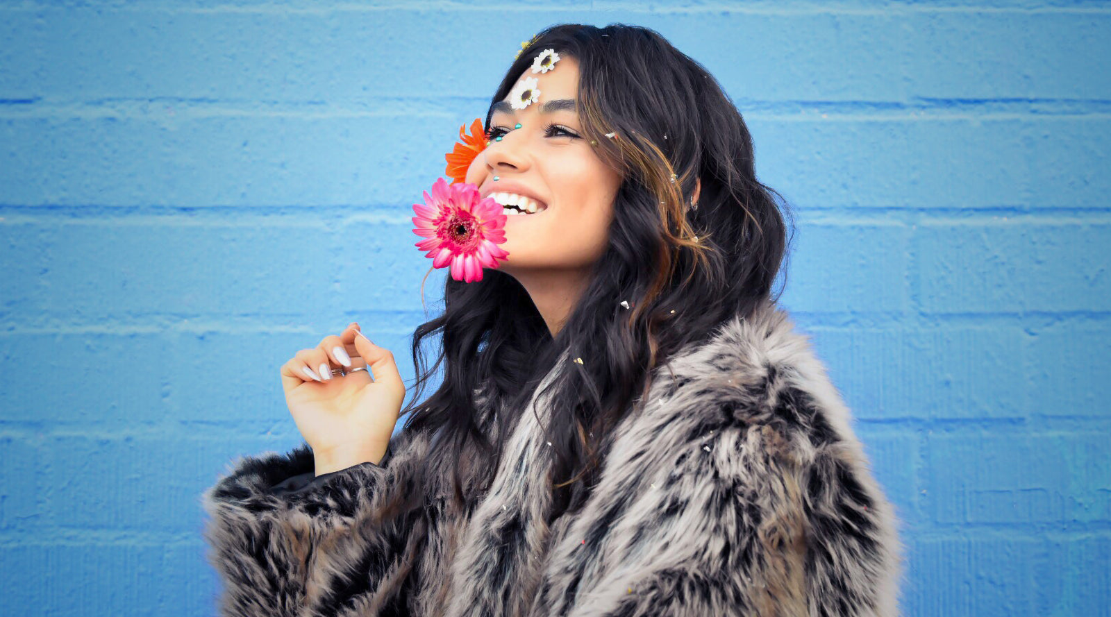 girl wearing faux fur coat while holding pink flower to her face
