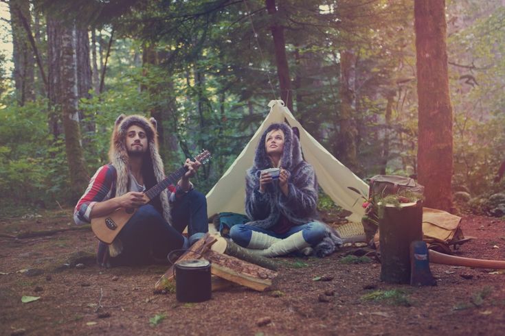 A man and woman sit outside their tent at a campsite. 