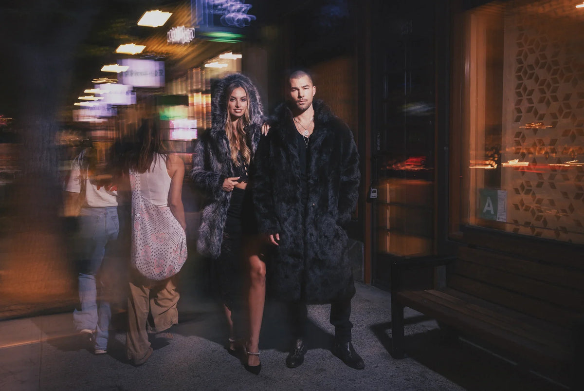 A man and a woman wear SpiritHoods faux fur coats walking down a busy street.