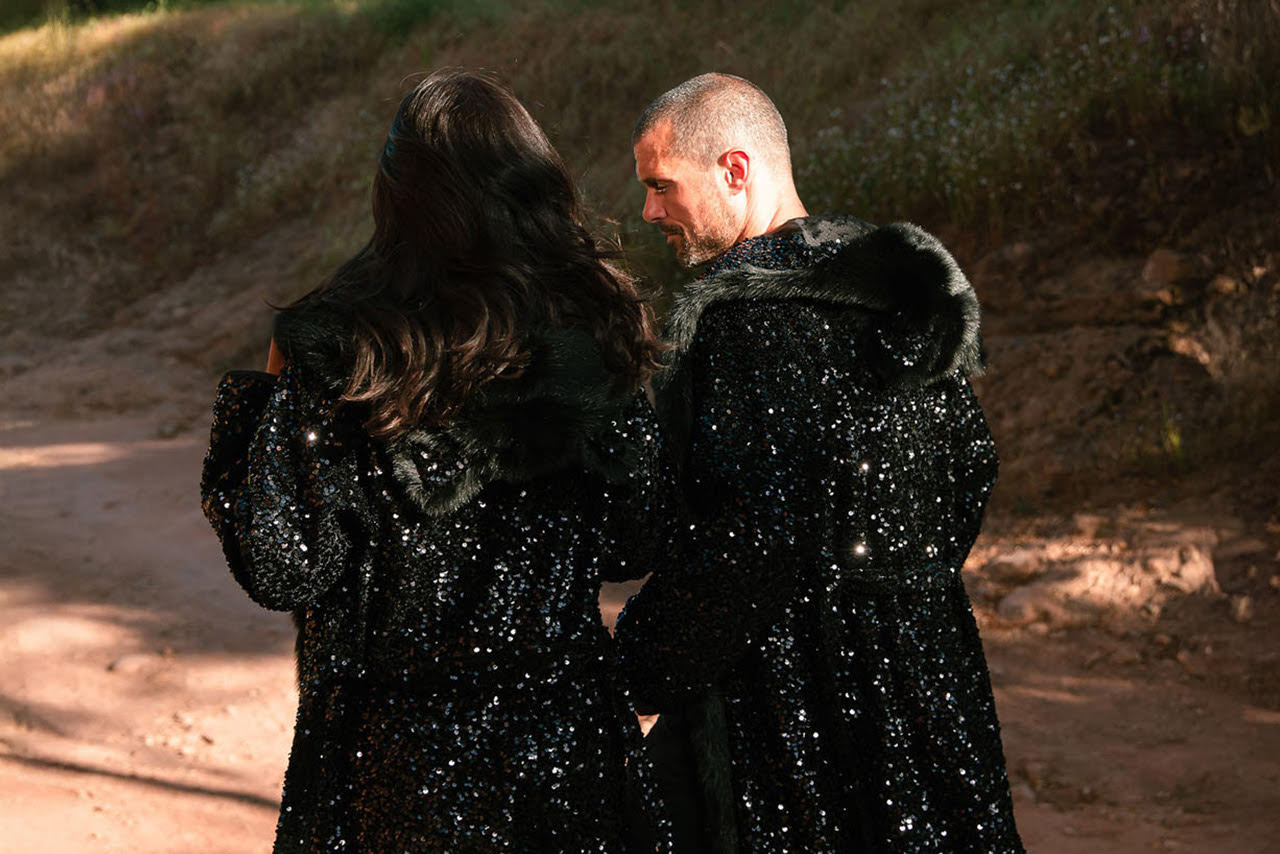 An  image of the back of a man and woman while they are wearing long  black sequin  faux fur coats by SpiritHoods. 