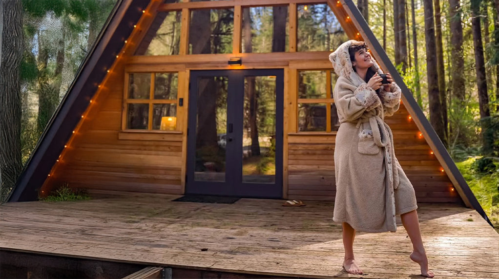 An image of a woman wearing the SpiritHoods wolverine faux fur robe outside a cabin.