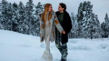 An image of a man and woman walking in the snow earring SpiritHood faux fur coats.