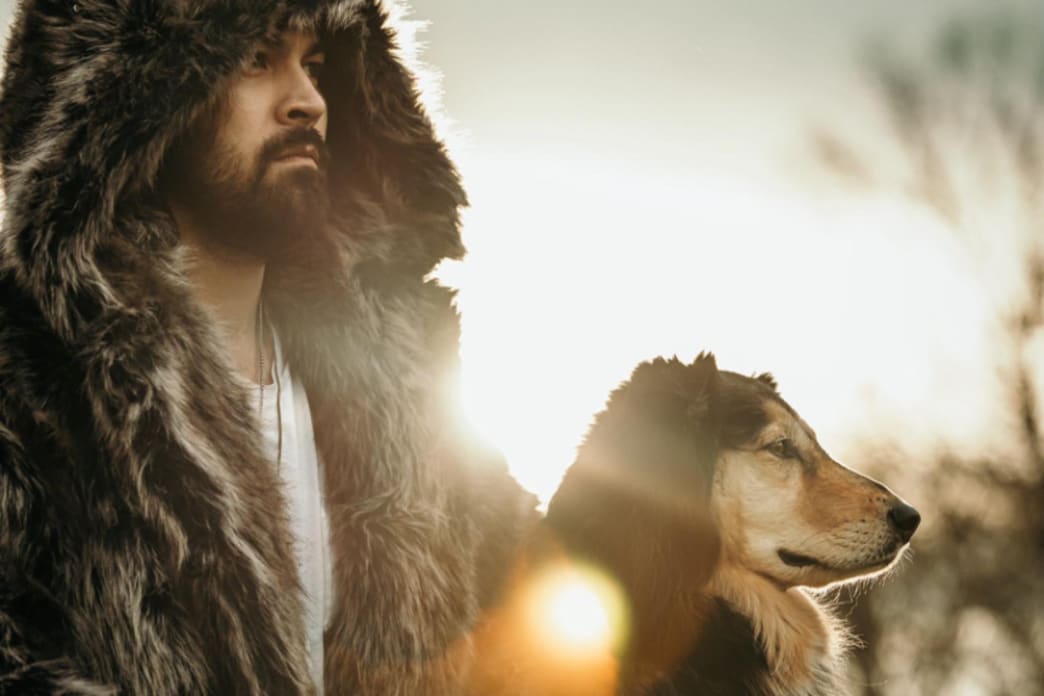 man wearing faux fur coat with dog standing next to him