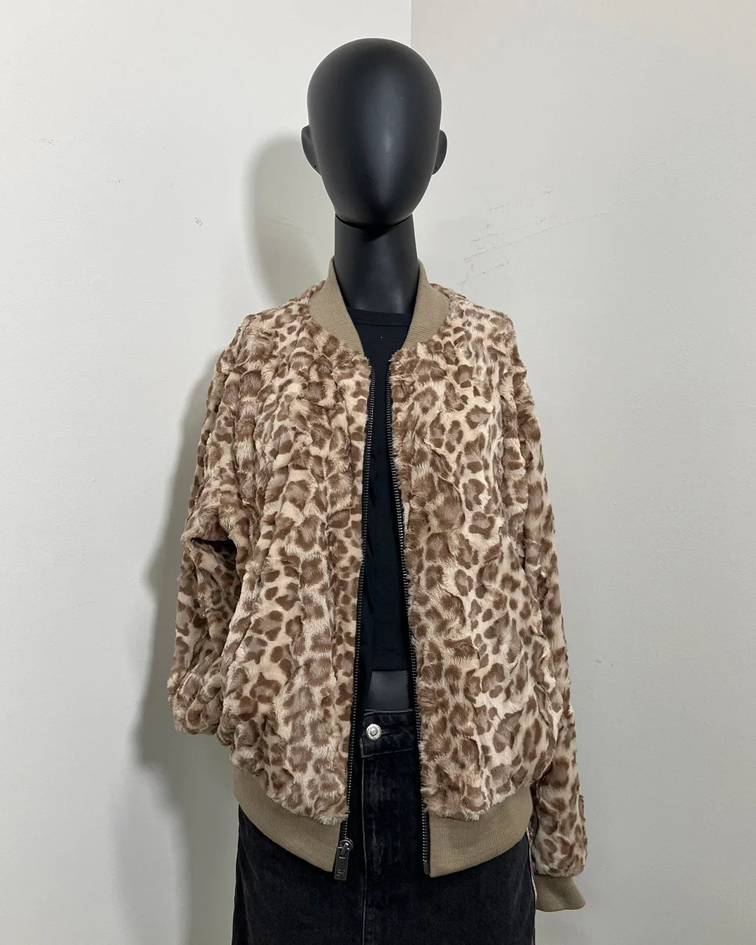 black mannequin wearing a tan strawberry leopard faux fur bomber jacket against a white wall