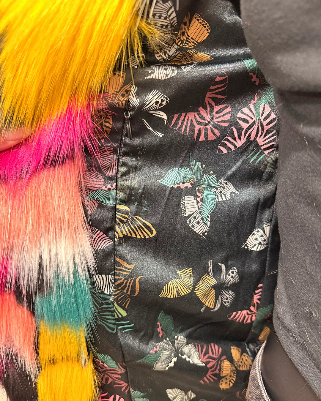 Close-up of a colorful fabric with butterfly pattern and fluffy multicolor accents. Also showing the inner secret zipper pocket on the butterfly calf length faux fur coat