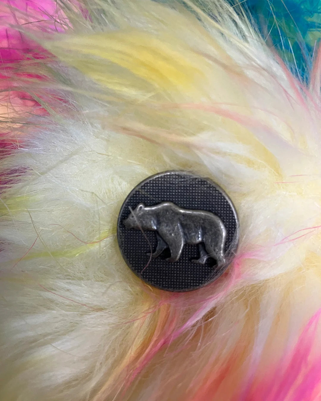 Metallic bear button on multicolored feathered background