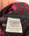 Close-up of a garment's interior neck label showing a leopard print pattern in black and magenta. A hand is holding the fabric open to reveal the white size and care tag.