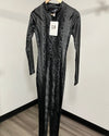 A black snakeskin-patterned long-sleeve jumpsuit hanging on a wooden hanger against a white wall, with a product tag attached.
