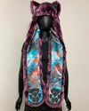 A hooded faux fur vest with cat ears, featuring a purple faux fur trim and a blue, orange, and purple tie-dye patterned lining with black paw prints near the bottom, displayed on a black mannequin.