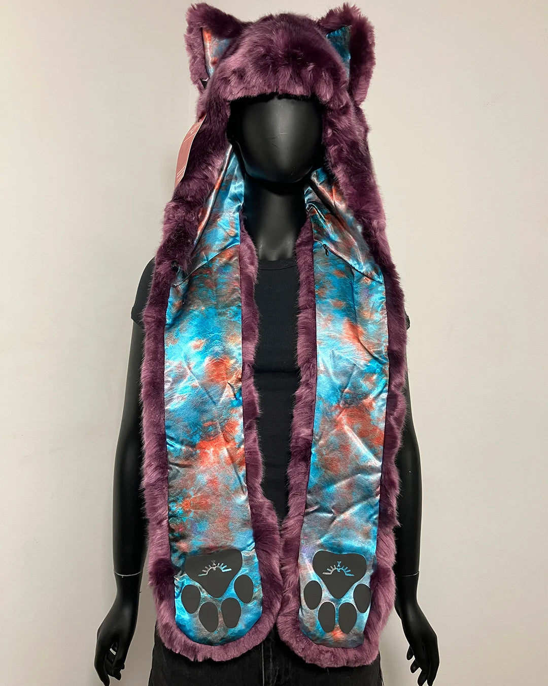 A hooded faux fur vest with cat ears, featuring a purple faux fur trim and a blue, orange, and purple tie-dye patterned lining with black paw prints near the bottom, displayed on a black mannequin.