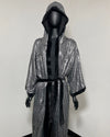 A hooded kimono robe with a silver sequined exterior and black satin lining, displayed on a black mannequin against a plain light gray wall.