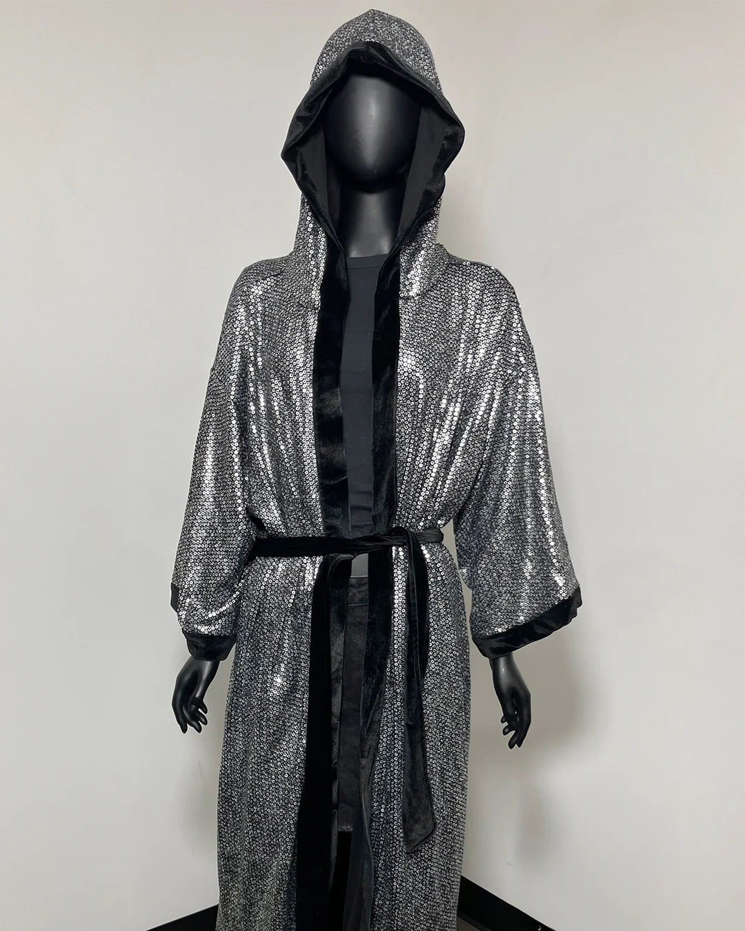 A hooded kimono robe with a silver sequined exterior and black satin lining, displayed on a black mannequin against a plain light gray wall.